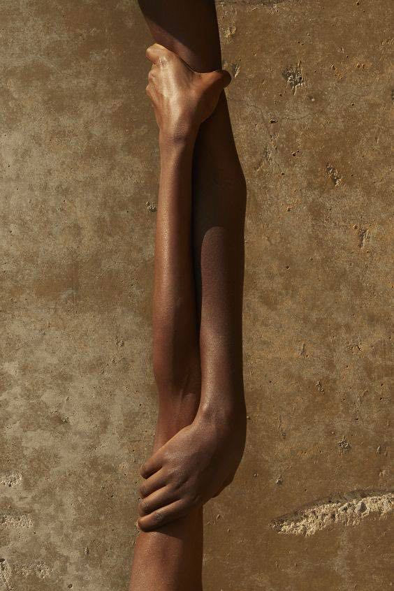 Two forearms clasping one another against a warm stone wall